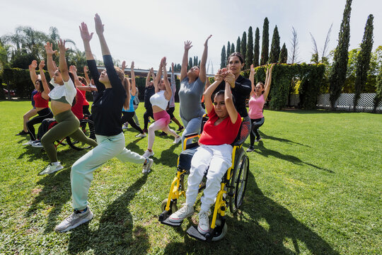 Large Group of Latin sporty multi age people stretching in training class next to mexican woman in wheelchair outdoors in a public park in Mexico Latin America. Diverse group in inclusion concept. 