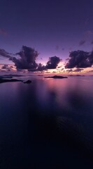 A serene seascape features islands at twilight, where purple and pink hues paint the sky and reflect on the calm water's surface