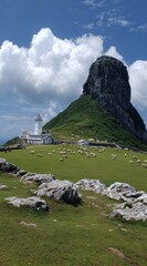 Idyllic seascape vista featuring a lighthouse atop a grassy hill with grazing sheep, set against a dramatic rocky mountain and bright, cloudy sky