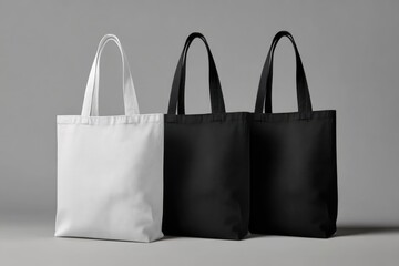 Three tote bags, one white, two black, stand on a gray background, showcasing their simple, reusable design