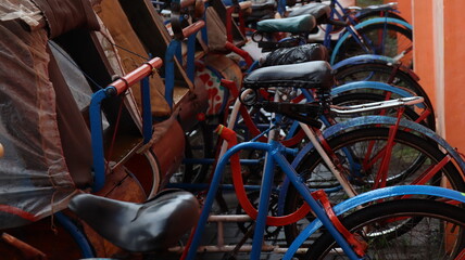Row of colorful traditional pedicabs with vintage bicycle design parked near orange wall in urban street
