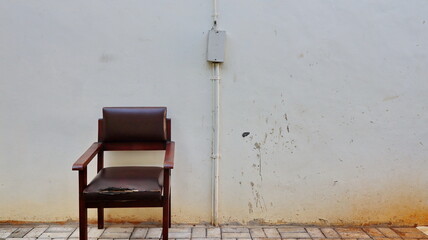 Old wooden chair with torn cushion placed against dirty stained wall on tiled floor in empty outdoor space