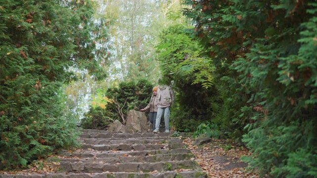 mother holds daughter hand while leading dog down stone staircase winding through lush green garden framed by autumn leaves wearing cozy jackets joyful family moment in serene outdoor pathway