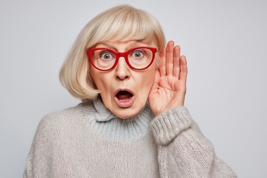 Shocked senior woman in red glasses trying to listen and eavesdrop on a rumor
