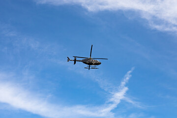 Black Helicopter in Flight Across Blue Sky with Scattered White Clouds