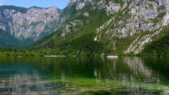 Calm water surface on lake Bohinj in Slovenia on a sunny morning. Peaceful natural surroundings with lake, mountains and trees. Eco tourism with electric boat on the lake. Paradise in Slovenian Alps.