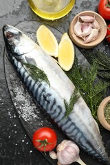 Fresh raw mackerel and spices on black table, flat lay. Seafood delicacies