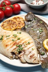 Tasty roasted flounder fish with herbs, lemon slices and tomatoes on light blue wooden table, closeup. Homemade seafood dish