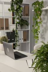 Stylish workplace with laptop, stationery and floral decor in office. Biophilic interior design