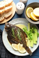 Tasty roasted flounder fish with celery served on blue table, flat lay. Homemade seafood dish