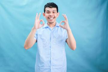 Naklejka premium Cheerful Young Man Giving a Positive Gesture in a Light Blue Background Delighting Viewers with His Smile