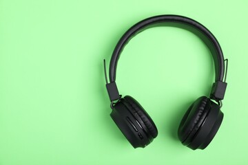 Pair of stylish black headphones on light green background, top view. Space for text