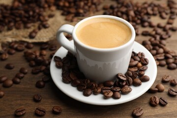 Aromatic coffee in cup and beans on wooden table, closeup