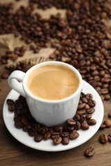 Aromatic coffee in cup and beans on wooden table, closeup