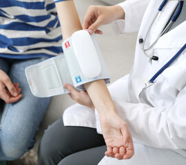 Obraz premium Doctor checking woman's heart rate and blood pressure via sphygmomanometer on sofa indoors, closeup