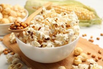 Tasty popcorn and corn kernels on white table, closeup