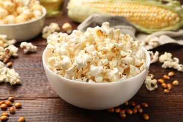 Tasty popcorn, corncob and corn kernels on wooden table, closeup