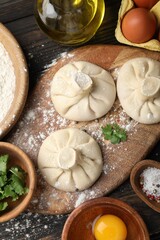 Uncooked khinkalis (dumplings) surrounded by ingredients on wooden table, flat lay