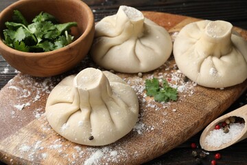 Uncooked khinkalis (dumplings), spices and parsley on wooden table, closeup