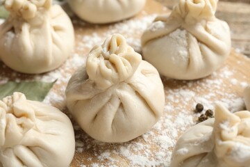 Uncooked khinkalis (dumplings) with flour on wooden table, closeup