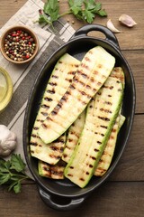 Delicious grilled courgette slices in baking dish and spices on wooden table, flat lay