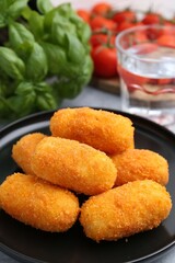 Delicious fried croquettes, glass of water, tomatoes and basil on table, closeup