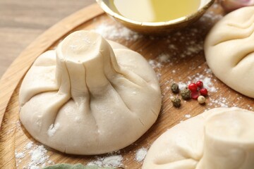 Uncooked khinkalis (dumplings) with peppercorns and flour on wooden table, closeup