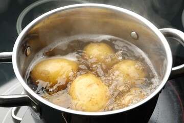 Young potatoes boiling in pot on stove, closeup