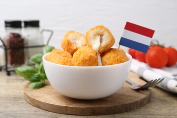 Delicious fried croquettes in bowl and flag of Netherlands on wooden table, closeup