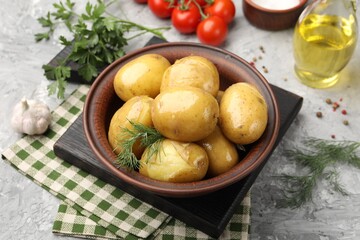 Tasty young boiled potatoes with dill, oil in bowl and products on grey textured table, closeup