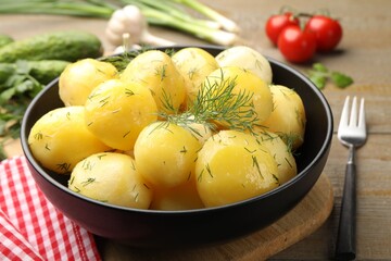 Tasty young boiled potatoes with dill and oil in bowl on wooden table, closeup