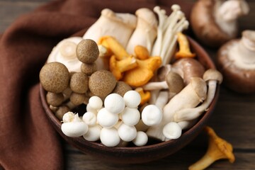 Different raw mushrooms in bowl on wooden table, closeup