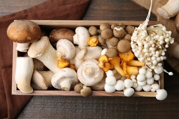 Different raw mushrooms and crate on wooden table, flat lay