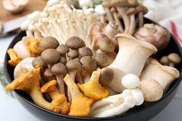 Different raw mushrooms in bowl on white table, closeup