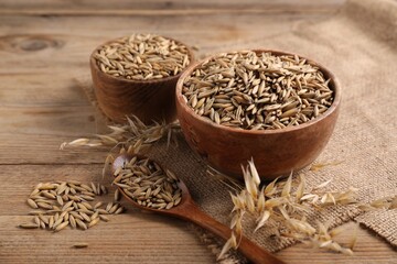 Oat grains, spoon, bowls, spikes and burlap cloth on wooden table, closeup