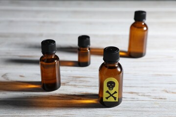 Bottles of poisons with warning sign on wooden table, closeup