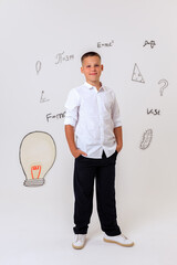 Thoughtful schoolboy in uniform sitting on wooden stool, student portrait with science and math formulas on white background, education and learning concept