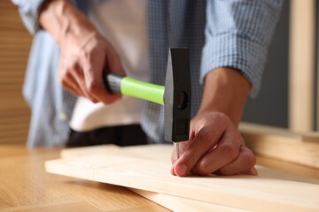 Man hammering nail into wooden plank indoors, closeup
