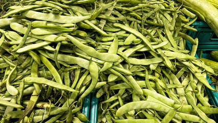 Close-up of fresh, long, green beans scattered on a market stall. Healthy eating and natural products.