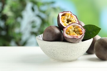 Fresh passion fruits in bowl on white wooden table outdoors, closeup. Space for text