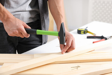 Man hammering nail into wooden plank indoors, closeup