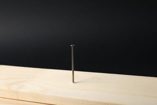 Metal nail in wooden plank on black background, closeup