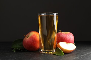 Fresh cider in glass, apples and green leaves on black table
