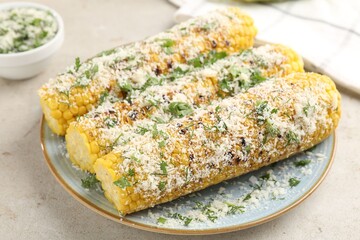Tasty grilled corncobs with parsley and cheese on light table, closeup