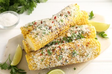 Tasty grilled corncobs with parsley, cheese and lime slices on white wooden table, closeup