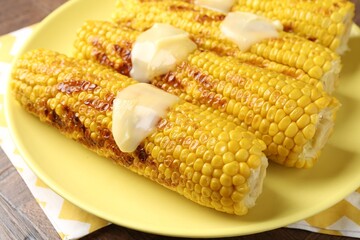 Tasty grilled corncobs with sauce on wooden table, closeup