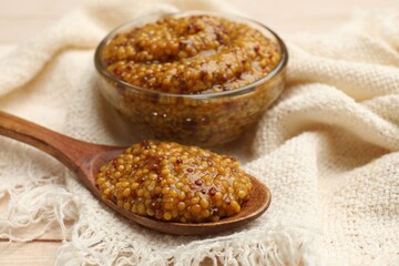 Whole grain mustard in glass bowl and spoon on table, closeup