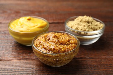 Different types of mustard on wooden table, closeup