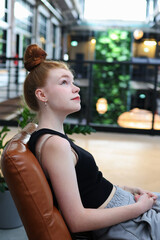 Casual girl with hoop earrings and neat bun hairstyle relaxing in contemporary space.