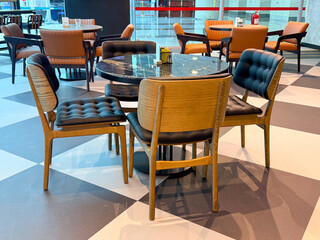 Round marble table surrounded by cushioned leather chairs in a public cafe. Social interaction, hospitality, and travel lifestyle represented through waiting, dining and leisure.